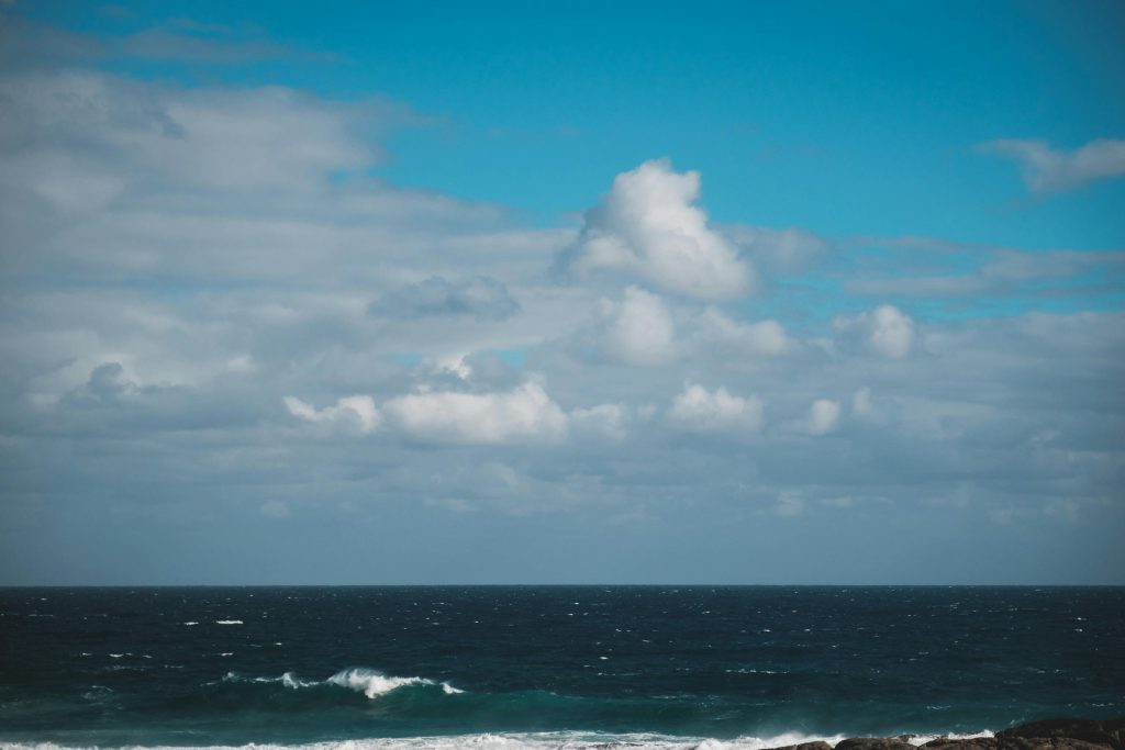 Expansive view of the ocean meeting the clear, blue sky with scattered clouds, creating a serene seascape.
